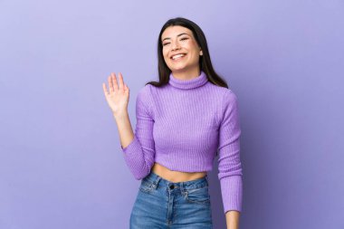 Genç esmer kadın, izole edilmiş mor arka planda mutlu bir ifadeyle selamlıyor.