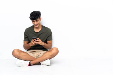 Yerde oturan genç Arjantinli adam cep telefonuyla mesaj yolluyor.