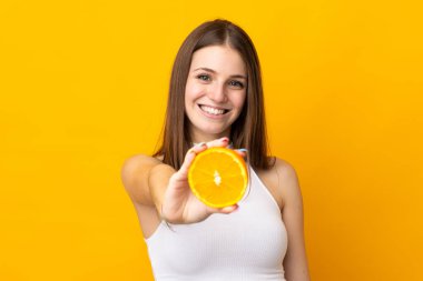 Turuncu arka planda portakal tutan beyaz bir kadın.
