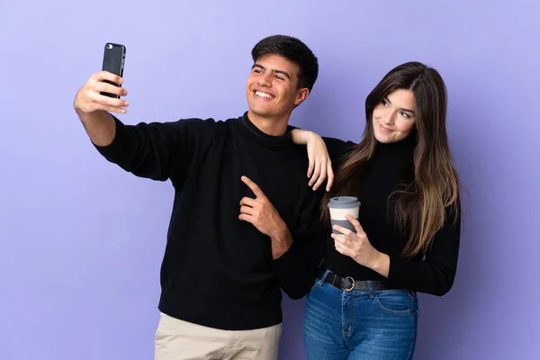 一对年轻夫妇在孤立的紫色背景上 用手机自拍 — 图库照片