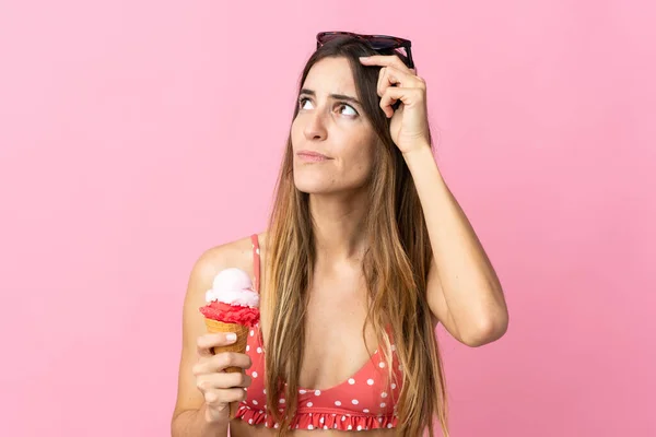 ピンクを背景にしたアイスクリームを持つ若い白人女性は疑問を持ち 顔の表情を混乱させます — ストック写真