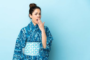 Kimono giyen bir kadın izole edilmiş arka planda esniyor ve ağzını eliyle açık tutuyor.