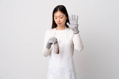 Çinli balıkçı önlük takıyor ve beyaz arka planda çiğ balık tutuyor. Durma hareketi yapıyor ve hayal kırıklığına uğruyor.