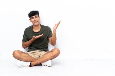 Genç Arjantinli adam yere oturmuş, davet edildiği için ellerini yana açıyor.