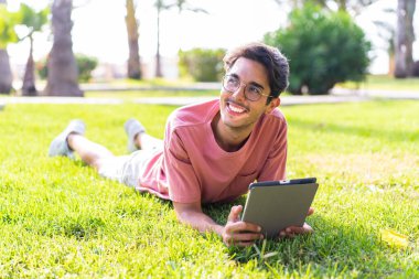 Parkta elinde tabletle gezen beyaz bir genç.