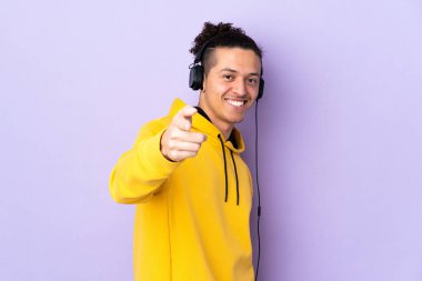 İzole edilmiş mor arka planda beyaz bir adam müzik dinliyor ve ön tarafı işaret ediyor.