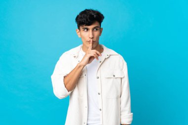 Arjantinli genç bir adam arka planda izole edilmiş. Parmağını ağzına koyduğunda sessizlik işareti gösteriyor.