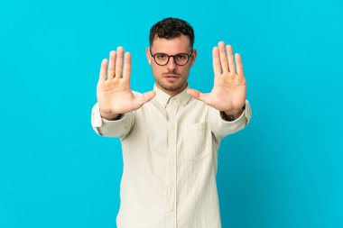 Beyaz tenli yakışıklı adam mavi arka planda izole edilmiş. Durma hareketi yapıyor ve hayal kırıklığına uğruyor.