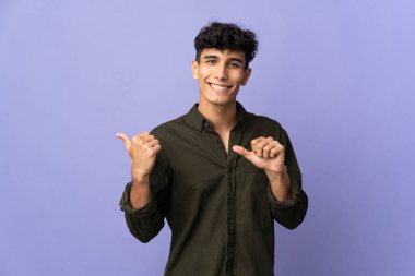 Arka planda izole edilmiş genç Arjantinli bir adam bir ürün sunmak için kenarı işaret ediyor