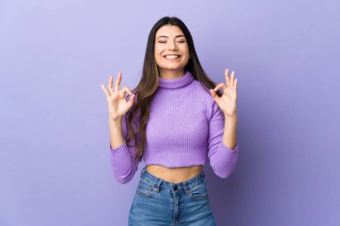 Zen pozisyonunda, izole edilmiş mor arka planda esmer bir kadın.