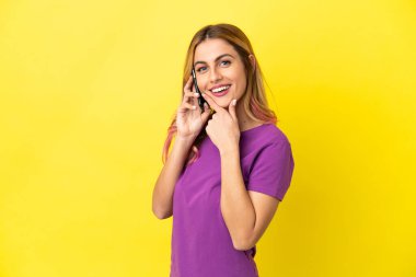 İzole edilmiş sarı arka planda cep telefonu kullanan genç bir kadın mutlu ve gülümsüyor.