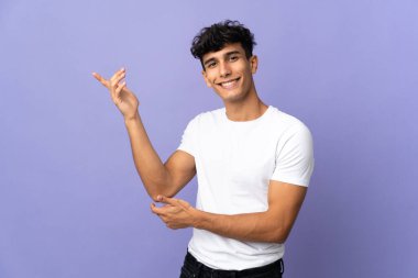 Arjantinli genç adam arka planda izole edilmiş. Davet etmek için ellerini yana uzatıyor.