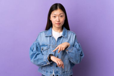 Mor arka planda kalan genç Çinli kız geç kalma jesti yapıyor.