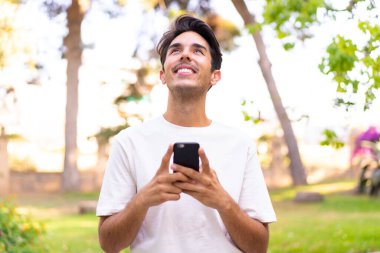 Parkta cep telefonu kullanan genç beyaz bir adam var.
