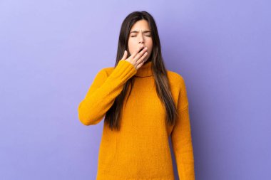 İzole edilmiş mor arka plan üzerinde Brezilyalı genç bir kız esniyor ve ağzını eliyle kocaman açık tutuyor.