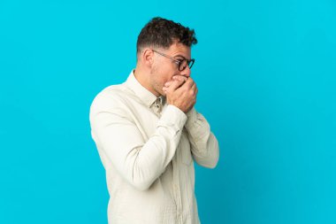 Beyaz tenli yakışıklı adam mavi arka planda izole edilmiş ağzını kapatıyor ve yan tarafa bakıyor.