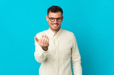 Beyaz tenli yakışıklı bir adam mavi arka planda izole edilmiş ve bizimle gelmesi için davet ediliyor. Gelmene sevindim.