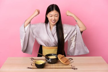 Kimono giyen ve şehriye yiyen genç Çinli kız güçlü bir jest yapıyor.