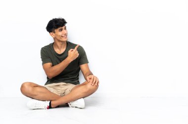 Genç Arjantinli bir adam yerde oturmuş arkasını işaret ediyor.