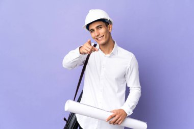 Genç mimar arka planda izole edilmiş, mutlu bir ifadeyle ön tarafı işaret ediyor.