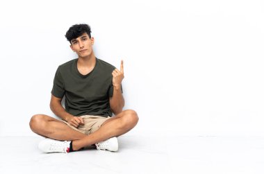 Genç Arjantinli bir adam yerde oturmuş işaret parmağıyla işaret ediyor. Harika bir fikir.