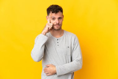 Beyaz tenli yakışıklı bir adam sarı arka planda izole edilmiş bir fikir düşünüyor.
