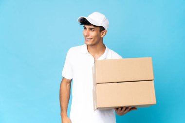 Teslimatçı Arjantinli adam mavi arka planda izole edilmiş, yana bakıyor ve gülümsüyor.