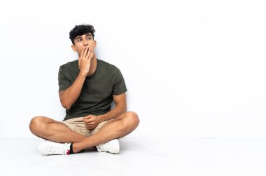 Genç Arjantinli adam yerde oturuyor esniyor ve ağzını eliyle kapatıyor.