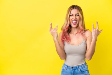 İzole edilmiş sarı arka planda genç bir kadın boynuz hareketi yapıyor.