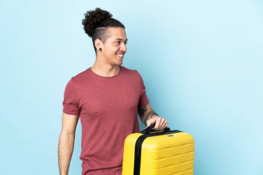 İzole edilmiş mavi geçmişi olan beyaz bir adam seyahat çantasıyla tatilde.