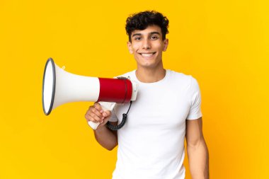 Arjantinli genç adam sarı arka planda, elinde bir megafonla ve sürpriz bir ifadeyle izole edilmiş.