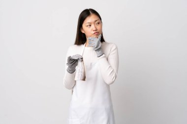 Çinli balıkçı önlük takıyor ve çiğ balığı izole edilmiş beyaz arka planda tutuyor. Şüpheleri var.