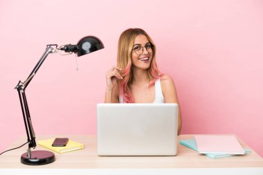 İşyerinde pembe arka planda dizüstü bilgisayarı olan genç bir bayan gülüyor.