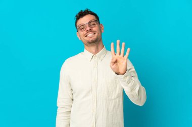 Genç, beyaz, yakışıklı bir adam mavi arka planda izole edilmiş mutlu ve parmaklarıyla dört kişi sayıyor.