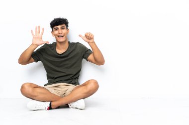 Genç Arjantinli adam yerde oturmuş parmaklarıyla altıya kadar sayıyor.