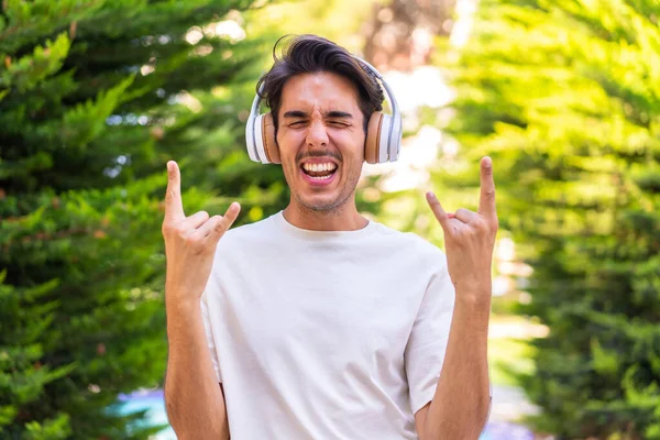 Jeune Homme Caucasien Dans Parc Écoutant Musique Faire Geste Rock — Photo