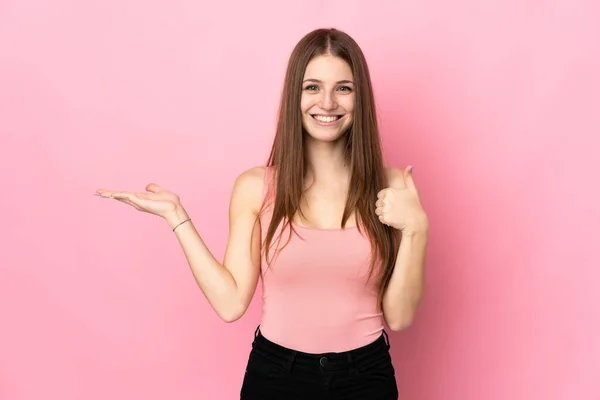 ピンクの背景に孤立した若い白人女性は 広告を挿入するには ヤシの上に架空のコピースペースを保持し 親指アップ — ストック写真