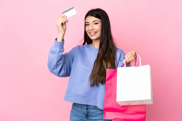 年轻的黑发女孩 背景是孤立的粉色 手里拿着购物袋和信用卡 — 图库照片