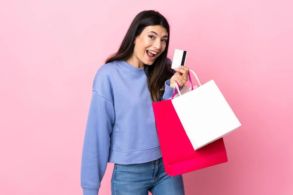 若いですブルネット女の子以上隔離されたピンクの背景を保持ショッピングバッグとクレジットカード — ストック写真