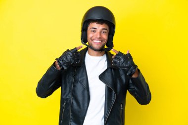 Motosiklet kasklı genç Brezilyalı adam sarı arka planda izole edilmiş bir şekilde baş parmak işareti yapıyor.