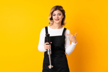 Sarı arka planda izole edilmiş, gururlu ve kendini beğenmiş el blenderi kullanan kız.