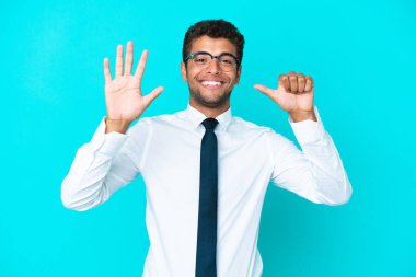 Genç Brezilyalı iş adamı mavi arka planda izole edilmiş. Parmakları olan altı kişi sayıyor.