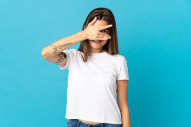 Genç Slovak kadın mavi arka planda izole edilmiş gözleri elleriyle kaplayan ve gülümseyen