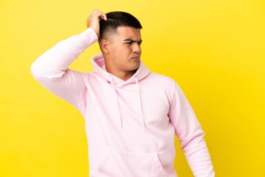 Genç, yakışıklı, soyutlanmış sarı arka planda, kafası kaşınırken şüpheleri olan bir adam.