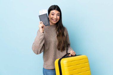 Genç esmer kız izole edilmiş mavi arka planda tatilde bavul ve pasaportla