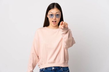 İzole edilmiş beyaz arka planı olan genç Çinli kız şaşırmış ve ön tarafı işaret ediyor.