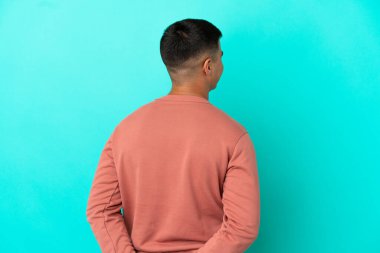 Genç ve yakışıklı bir adam izole edilmiş mavi arka planda ve geriye bakıyor.