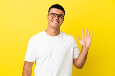 Genç yakışıklı adam izole edilmiş sarı arka planda mutlu bir ifadeyle selamlıyor.