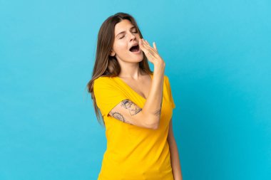 Genç Slovak kadın mavi arka planda izole edilmiş esniyor ve geniş ağzı eliyle kapatıyordu.