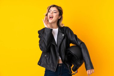 Sarı arka planda izole edilmiş motosiklet kaskı tutan genç bir kadın ağzı açık bağırıyor.